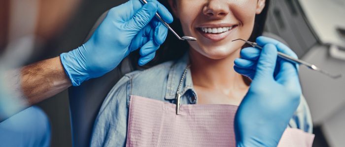 Young adult woman smiling while a dentist examines her mouth with dental tools