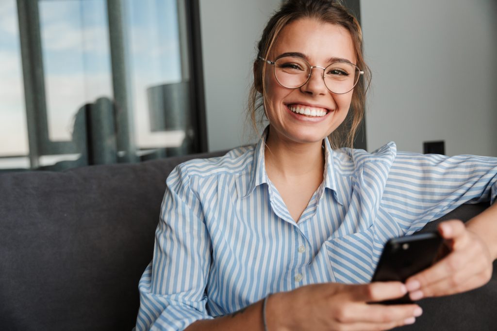Image Of Happy Young Woman In Eyeglasses Smiling And Using Cellp